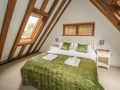 A bedroom with a double bed with green bedspread and pillows white bedside tables and lamps under wooden beams and a window at Trevinny Lodge No 37 Davidstow near Boscastle