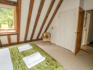 A bedroom with a bed covered in green bedding and white towels a wicker chair a window and wooden beams at Trevinny Lodge No 37 Davidstow near Boscastle