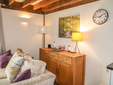 A living room corner with a beige sofa and wooden cabinet with lamps and decorative items at Trevinny Lodge No 37 Davidstow near Boscastle