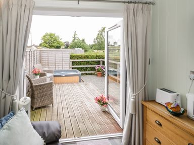 A patio with wicker chairs and a hot tub seen from inside a room with drawers and a toaster at Alstroemeria Bretforton near Evesham