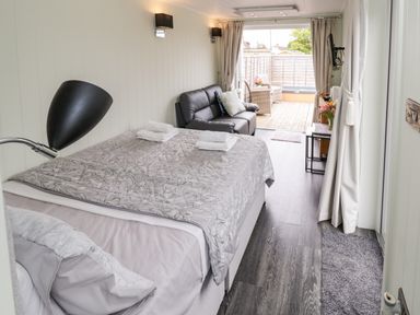 A bedroom with a bed a sofa and an open door leading to a deck with chairs at Alstroemeria in Bretforton near Evesham