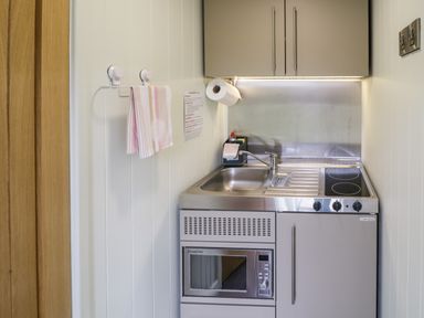 A small kitchen area with sink, stovetop, microwave, cabinets, and a towel hanging on the wall at Alstroemeria Bretforton near Evesham