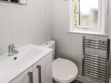 A bathroom with a white sink cabinet a toilet a small window and a heated towel rail at Alstroemeria Bretforton near Evesham