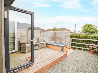 An outdoor patio with two wicker chairs a table a hot tub wooden fencing and gravel ground at Alstroemeria Bretforton near Evesham