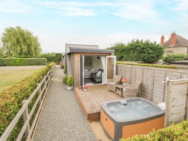 A small modern cabin with open doors leading to a deck with wicker chairs and a hot tub at Alstroemeria Bretforton near Evesham