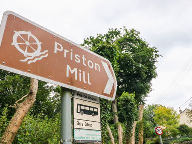 A road sign pointing to Priston Mill and a bus stop sign for Priston School in a rural setting at Pheasant Cottage Priston Village BATH