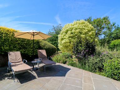 A garden with sun loungers and an umbrella at Pheasant Cottage in Priston Village, BATH