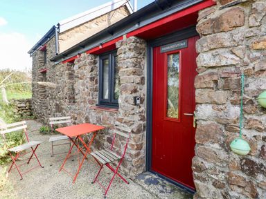 An outdoor area with a red door and stone wall at Farmhand Cottage near Narberth