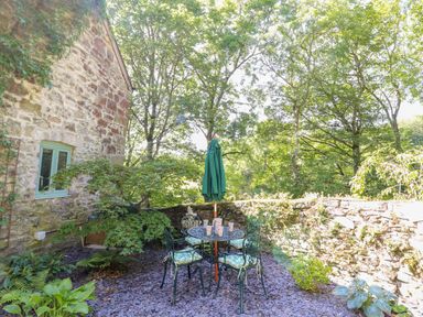 An outdoor patio with a round table and chairs under an umbrella next to a stone wall at The Old Coach House in Llanarmon-Yn-Ial