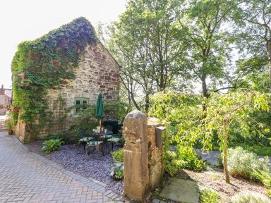An outdoor seating area with a table and chairs near a stone building covered in ivy at The Old Coach House in Llanarmon-Yn-Ial