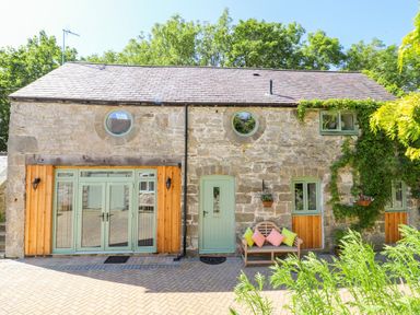 A stone house with green doors and windows with a bench and colorful cushions outside at The Old Coach House in Llanarmon-Yn-Ial
