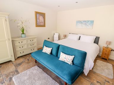 A bedroom with a double bed blue loveseat and dresser at The Old Coach House in Llanarmon-Yn-Ial