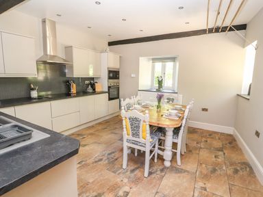 A kitchen with a wooden dining table and white chairs next to a countertop with cabinets at The Old Coach House in Llanarmon-Yn-Ial