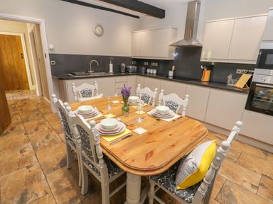 A kitchen with a wooden dining table set for six and white cabinets at The Old Coach House in Llanarmon-Yn-Ial