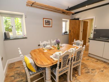 A dining area with a wooden table set for six and white chairs with patterned cushions at The Old Coach House in Llanarmon-Yn-Ial