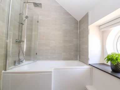 A bathroom with a bath and shower next to a round window with a plant at The Old Coach House in Llanarmon-Yn-Ial