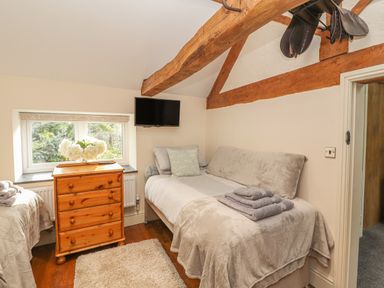 A bedroom with two beds a wooden chest of drawers under a window and a wall mounted television at The Old Coach House in Llanarmon-Yn-Ial