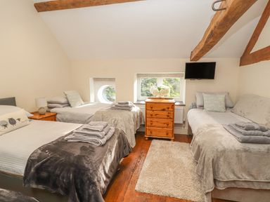 A bedroom with three single beds a wooden chest of drawers a wall-mounted television and exposed wooden ceiling beams at The Old Coach House in Llanarmon-Yn-Ial