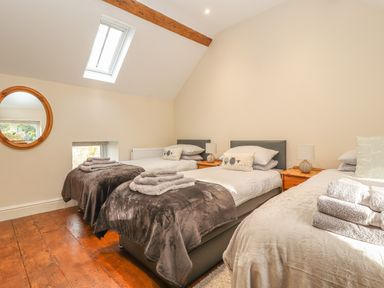 A bedroom with three single beds with towels on them and a round mirror on the wall at The Old Coach House in Llanarmon-Yn-Ial