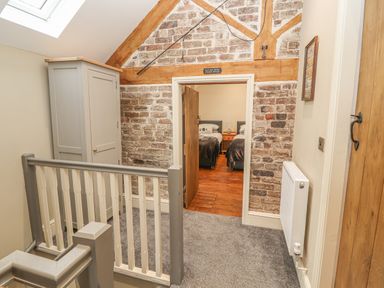A hallway with gray and white railing a gray wardrobe and brick walls leading to a bedroom at The Old Coach House in Llanarmon-Yn-Ial