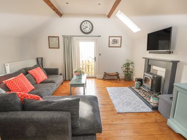 A living room with grey sofas and red cushions a coffee table and a fireplace with a television above at The Old Coach House in Llanarmon-Yn-Ial