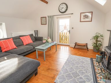 A sitting room with a gray sofa red cushions a coffee table a wall clock and a fireplace at The Old Coach House in Llanarmon-Yn-Ial