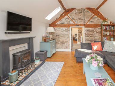 A living room with exposed brick wall a fireplace a grey sofa and a turquoise coffee table at The Old Coach House Llanarmon-Yn-Ial