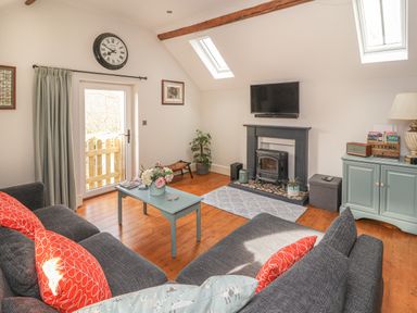 A living room with a gray sofa with red pillows a blue coffee table flowers a fireplace and a TV at The Old Coach House Llanarmon-Yn-Ial