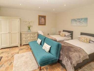 A bedroom with two beds a teal sofa a dresser with a plant and wardrobe at The Old Coach House in Llanarmon-Yn-Ial