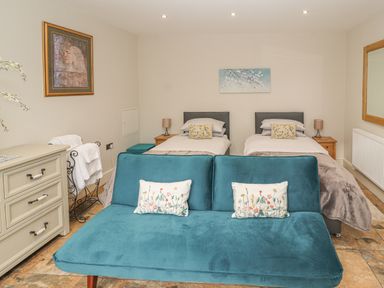 A bedroom with two single beds a blue sofa a chest of drawers and wall art at The Old Coach House in Llanarmon-Yn-Ial