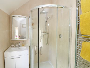 A bathroom with a glass shower enclosure yellow towels on a heated towel rail and a white sink cabinet at The Old White Cottage in Shillelagh County Wicklow
