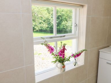A window with purple flowers in a vase on the sill in a tiled room at The Old White Cottage in Shillelagh County Wicklow