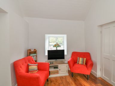 A small sitting room with two red armchairs a television on a cabinet and a small bookshelf at The Old White Cottage in Shillelagh County Wicklow