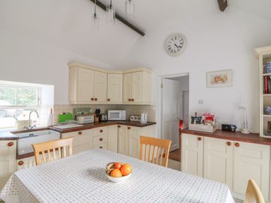 A kitchen with cream cabinets wooden countertops a table with fruit in a bowl and a window at The Old White Cottage in Shillelagh County Wicklow