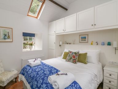 A bedroom with a double bed with white bedding and floral cushions blue blanket and built-in white cabinets at The Old White Cottage in Shillelagh County Wicklow
