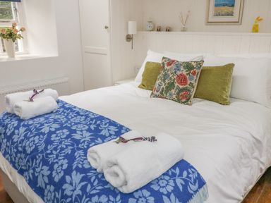 A bedroom with a bed with white sheets blue floral blanket and pillows at The Old White Cottage in Shillelagh County Wicklow