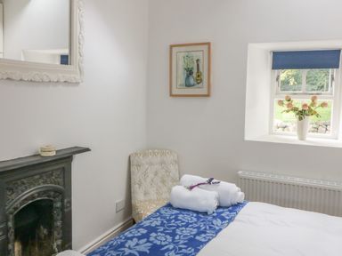 A bedroom with a bed covered with white and blue blankets a small window with flowers on the sill a decorative fireplace and a chair at The Old White Cottage in Shillelagh County Wicklow