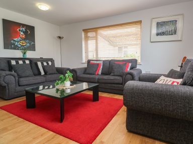 A living room with three grey sofas a black coffee table on a red rug and artwork on the walls at Tremar Carbis Bay