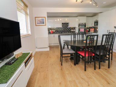 A kitchen with black dining table and chairs a television and white cabinets at Tremar in Carbis Bay
