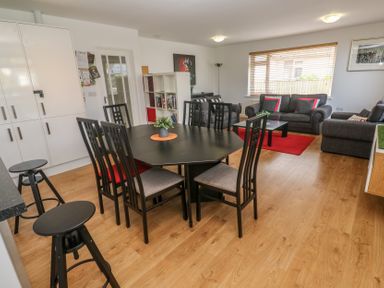 A dining area with a black table and six chairs next to a living room with gray sofas and a red rug at Tremar in Carbis Bay