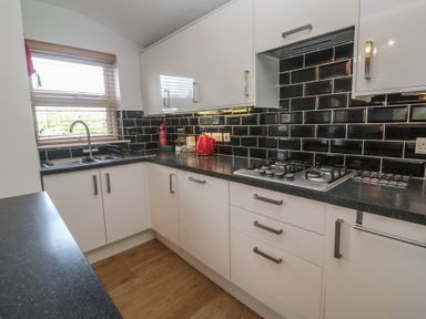 A kitchen with white cabinets black countertops a gas stove and a window with blinds at Tremar in Carbis Bay