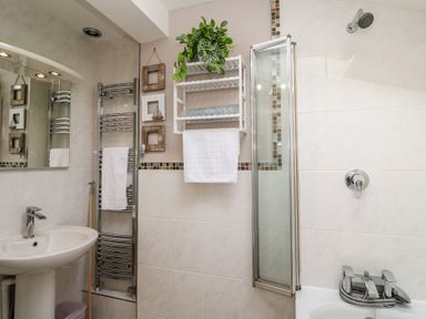 A bathroom with a sink a mirror a towel rack a shelf with a plant and towels and a bathtub with a showerhead at Tremar in Carbis Bay