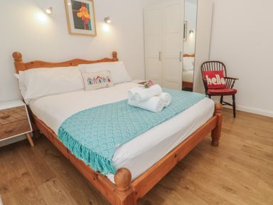 A bedroom with a wooden bed and blue blanket white towels wardrobe and a wooden chair with a red cushion at Tremar in Carbis Bay