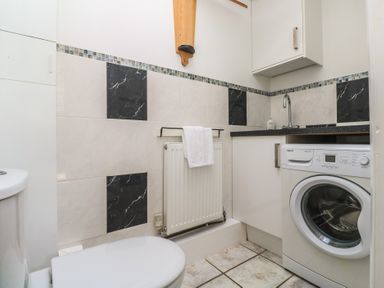 A small laundry room with a washing machine sink countertop and a radiator with a towel at Tremar in Carbis Bay