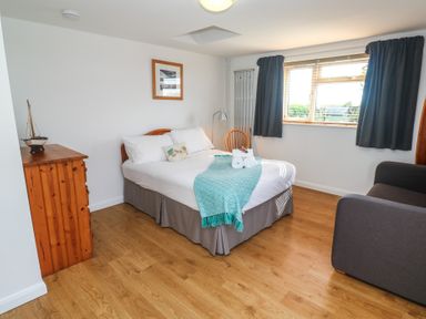A bedroom with a double bed wooden chest of drawers a chair and a window with curtains at Tremar in Carbis Bay