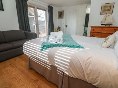 A bedroom with a bed with towels a sofa wooden floor and a dresser with a model boat at Tremar Carbis Bay