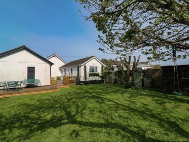 A backyard with green grass a tree with a swing a white building with a wooden deck and outdoor furniture at Tremar in Carbis Bay