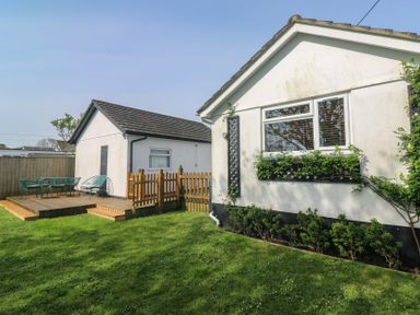 A backyard with green grass a wooden deck with chairs and table and two white buildings at Tremar in Carbis Bay