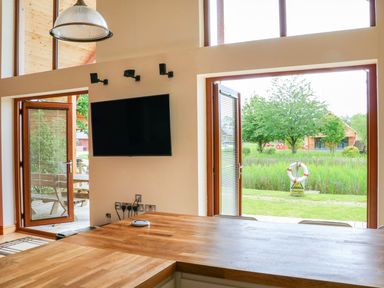 A room with wooden countertops a wall-mounted tv and open doors leading outside to grass and trees at Dorado Lodge in Thorpe-on-the-Hill
