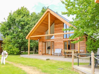 A wooden cabin with a covered porch and outdoor seating surrounded by trees at Dorado Lodge in Thorpe-on-the-Hill